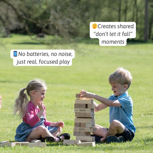 Two children playing wooden tumble tower stacking game on grass 