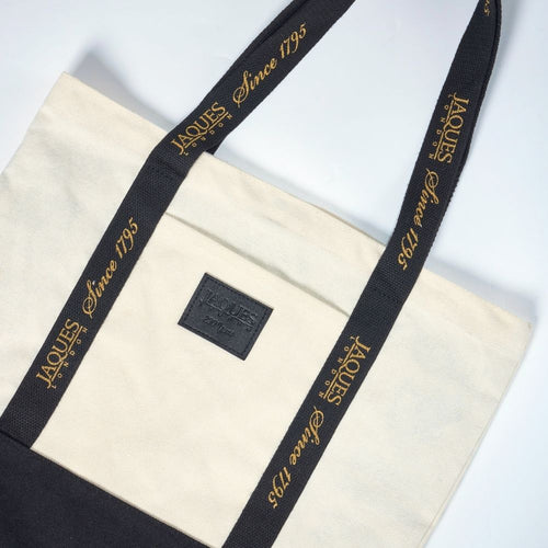 Beige tote bag with black strap featuring 'Jaques' branding on a white background 