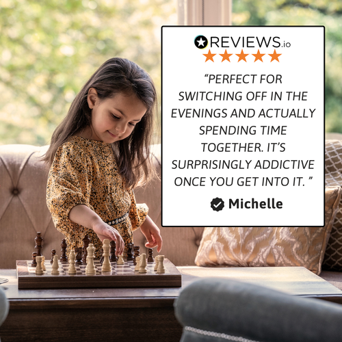 A young girl playing chess indoors at a table with a wooden folding chess set, featuring a customer review text overlay describing the quality and enjoyment of the chess set. 
