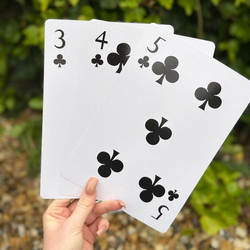 Hand holding three playing cards with black club symbols on a natural background