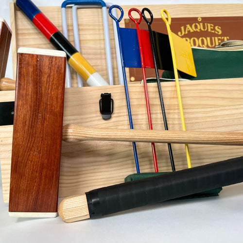 Close-up of a wooden croquet set with mallets and balls on a white surface, branded 'Jaques'. 