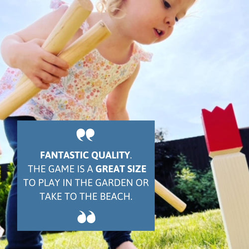 Young child holding two wooden throwing batons while setting up the Jaques of London Kubb Set, with blue review box saying “Fantastic quality. The game is a great size to play in the garden or take to the beach.” 