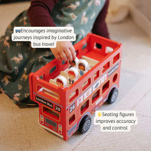 Child playing with a red wooden double-decker London bus toy, placing small wooden passenger figures inside, with text about encouraging imaginative journeys inspired by London bus travel. 