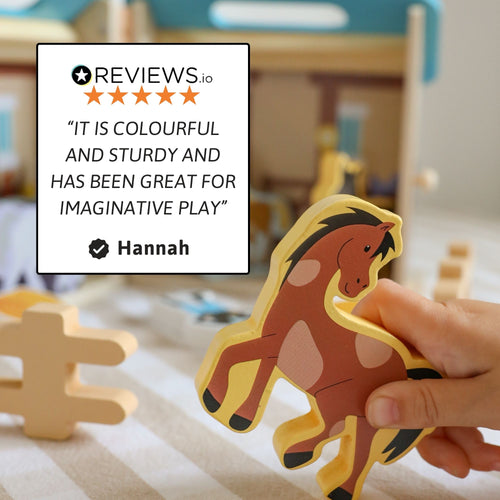 Close-up of a hand holding a wooden horse figure from the stable set with a customer review quote praising its colorful design and imaginative play value. 