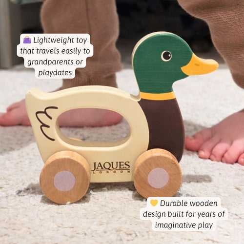 Wooden toy duck with a cart, featuring Jaques of London branding, on a carpeted floor. 