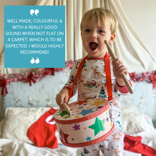 Smiling toddler wearing toy drum with red strap, featuring review text praising the drum’s colour and sound quality. 