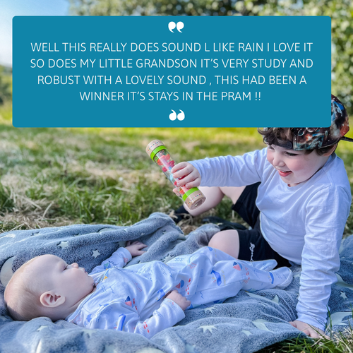 Older child holding the rain sound maker above a baby lying on a blanket outdoors, with a customer review quote displayed above 