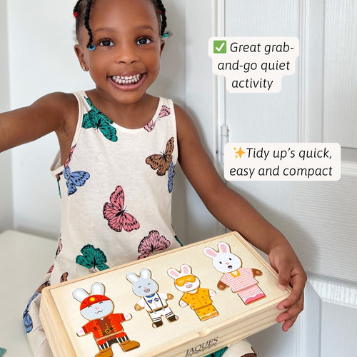 Child holding a wooden toy with rabbit figures, smiling, against a white wall.