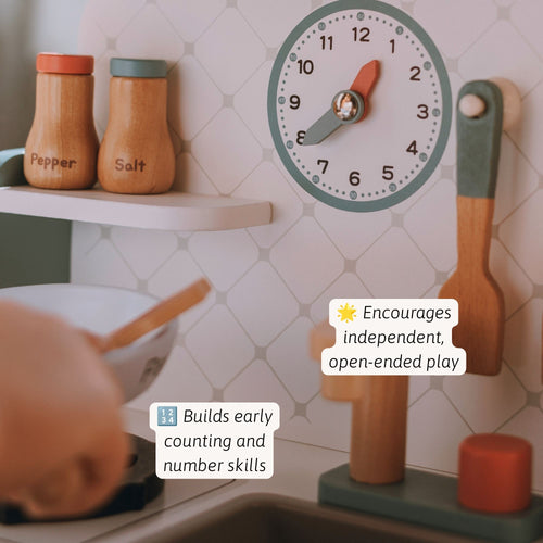 A children's wooden kitchen play set shown in use, with a round clock, utensils, spice jars, and a countertop scene. Text callouts mention early counting and number skills and independent play.