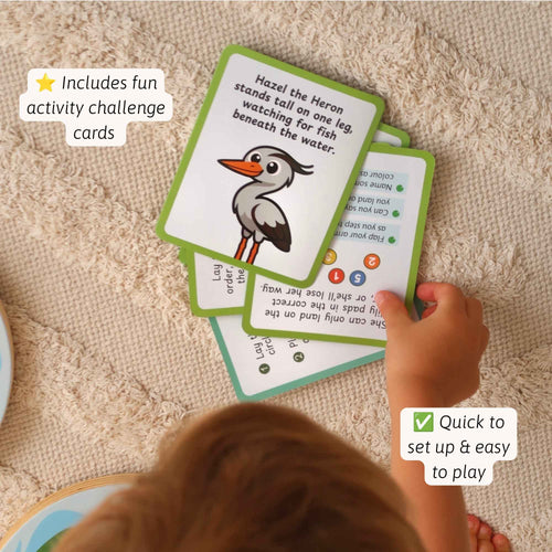 A child's hand is shown interacting with green and white educational cards featuring a heron illustration, placed on a beige textured blanket. White text overlays highlight included activity challenge cards and quick setup. 