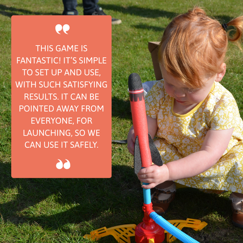 A small child sits on the grass while holding a foam rocket on the launcher, with a large review box describing how simple and satisfying the rocket toy is to use. 