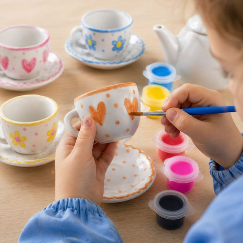 Child painting a ceramic cup with colourful paint on a wooden table. 