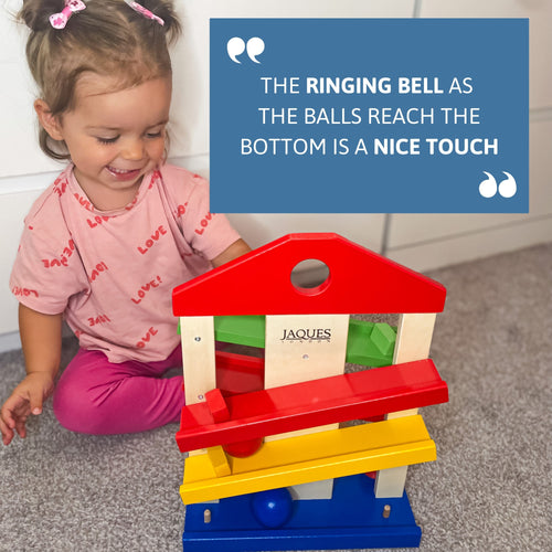 Smiling toddler playing indoors with Jaques wooden ramp toy – the ringing bell at the bottom adds a fun sensory touch to learning play. [filll]