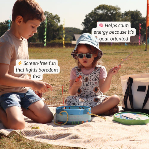 Two children sitting outdoors playing with a blue magnetic frog fishing game, using wooden rods to catch colourful wooden frogs, with feature callouts about screen-free and calming play 
