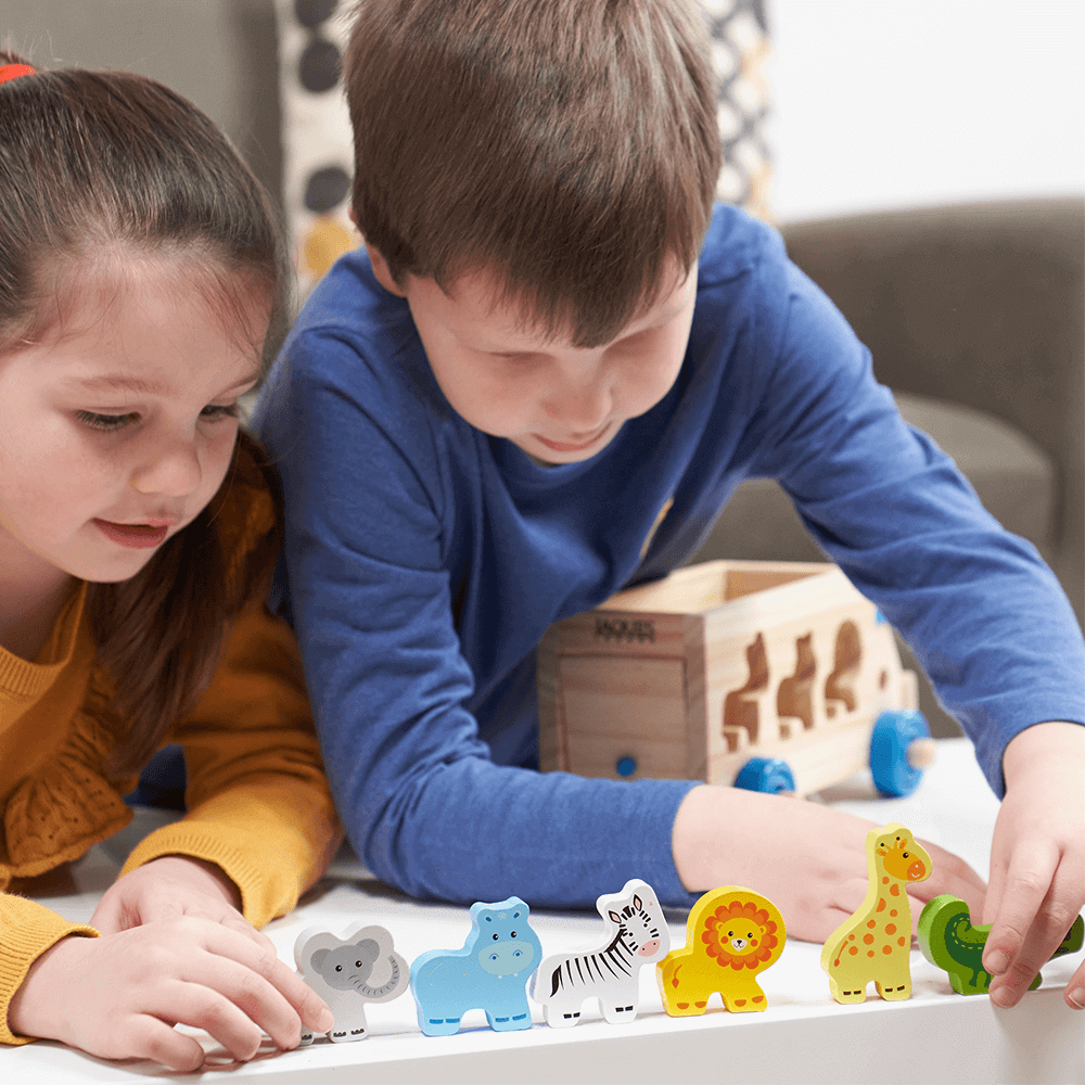  Girl and boy playing with the animals and the wooden shape sorter. Lining the animals; (left to right) elephant, hippo, zebra, lion, giraffe, crocodile, up on the edge of the table