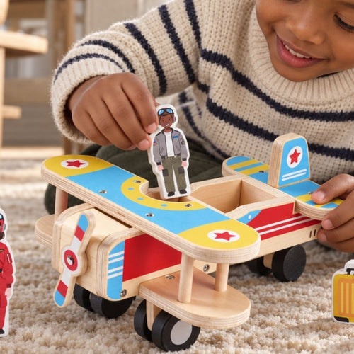 A child wearing a cream knit sweater with navy stripes is playing with a wooden toy biplane on a beige carpet. The toy plane has a natural wood body with bright blue, red, and yellow painted details, black wheels, and one pilot. 