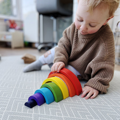 Child playing with a rainbow-colored toy on a carpeted floor. 