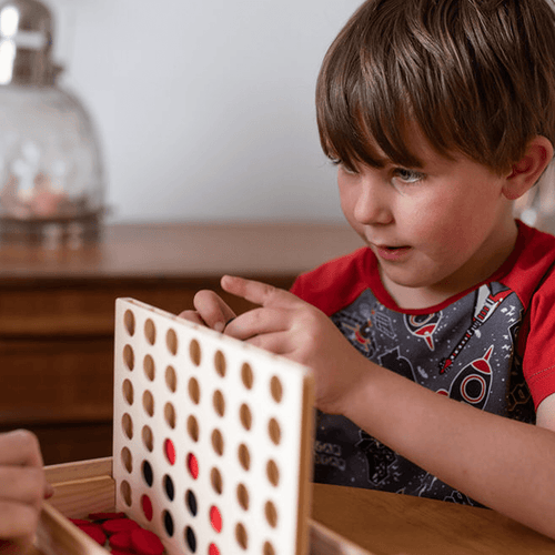  Young boy playing with the game and about to put counter in top of the Four in a Row Game