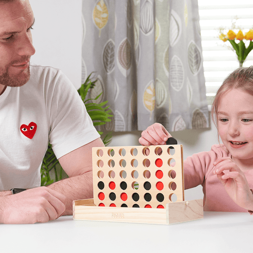  Girl placing black counter into the Four in a Row Board while playing at the table with Dad 