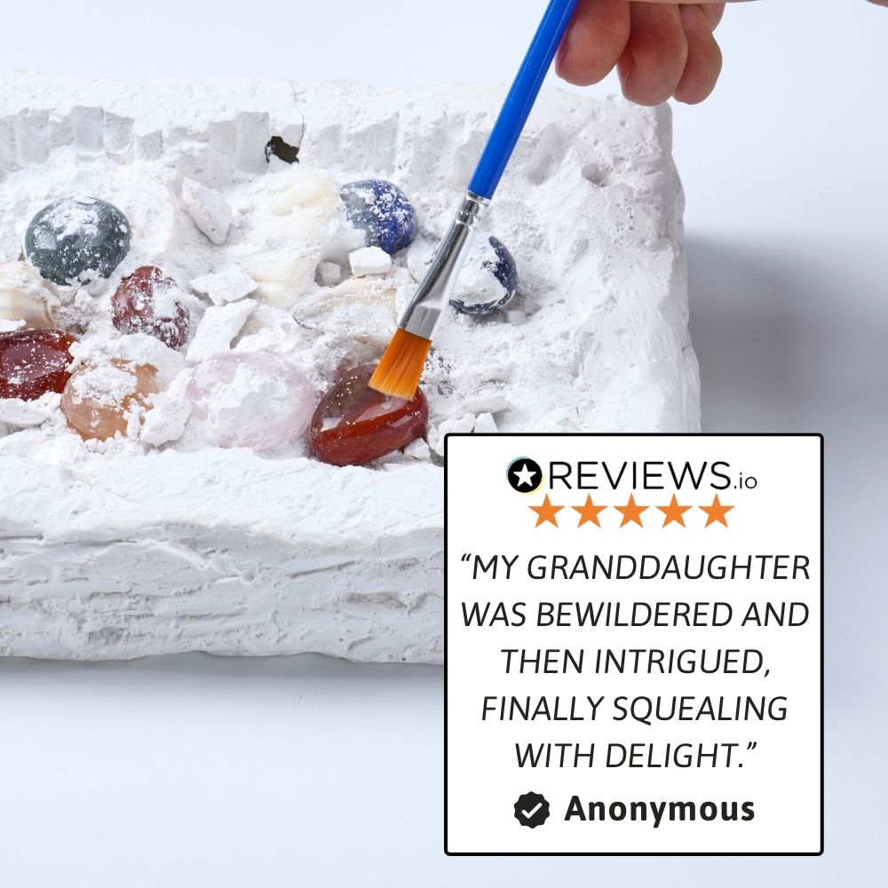 Hand using a blue paintbrush to decorate a cake with colorful candies on a white background, featuring a five-star review. 