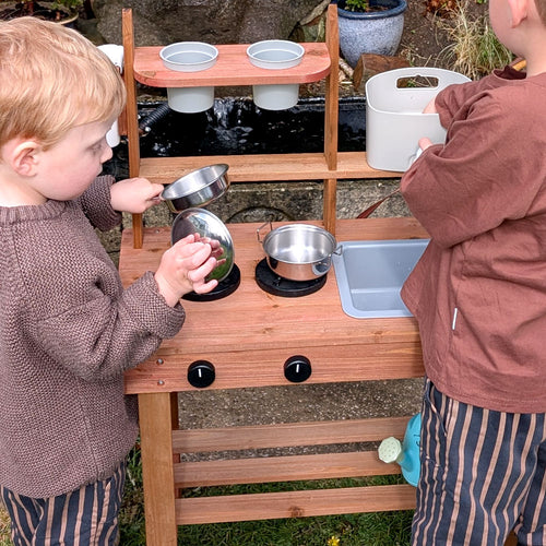 Children's playing with wooden mud kitchen pans 