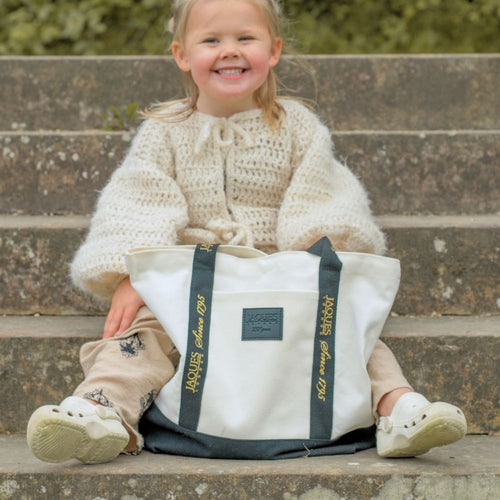 Child sitting on steps holding a white bag with branding. 