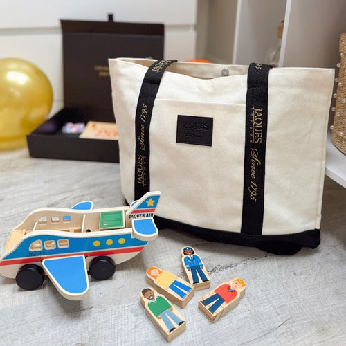Wooden airplane toy and figurines next to a white bag with branding on a light surface.  