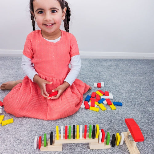 Little girl setting up a rally with colourful dominoes  