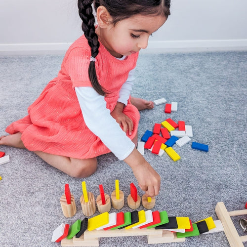 Little girl setting up a rally with colourful dominoes om grey carpet 