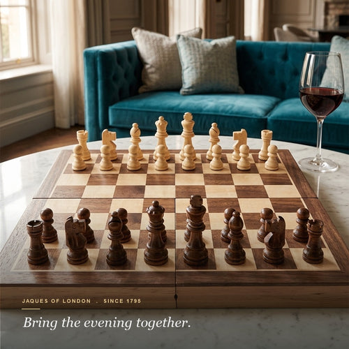 Jaques folding chess set set up on a marble table with red wine and a velvet sofa 