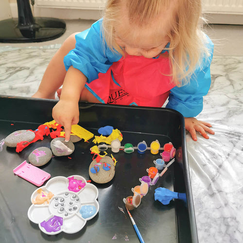  Girl looking down finger painting one of the rocks with white paint 
