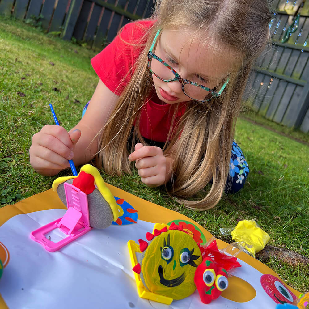  Zoom in of girl looking at the rock while painting it outside on the grass