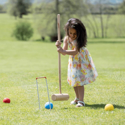 Girl holding croquet mallet to hit blue ball through hoop 